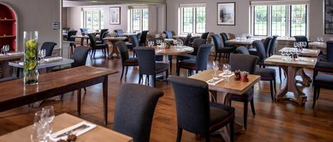 A spacious restaurant with multiple dining tables and chairs, large windows providing natural light, and a modern interior design.