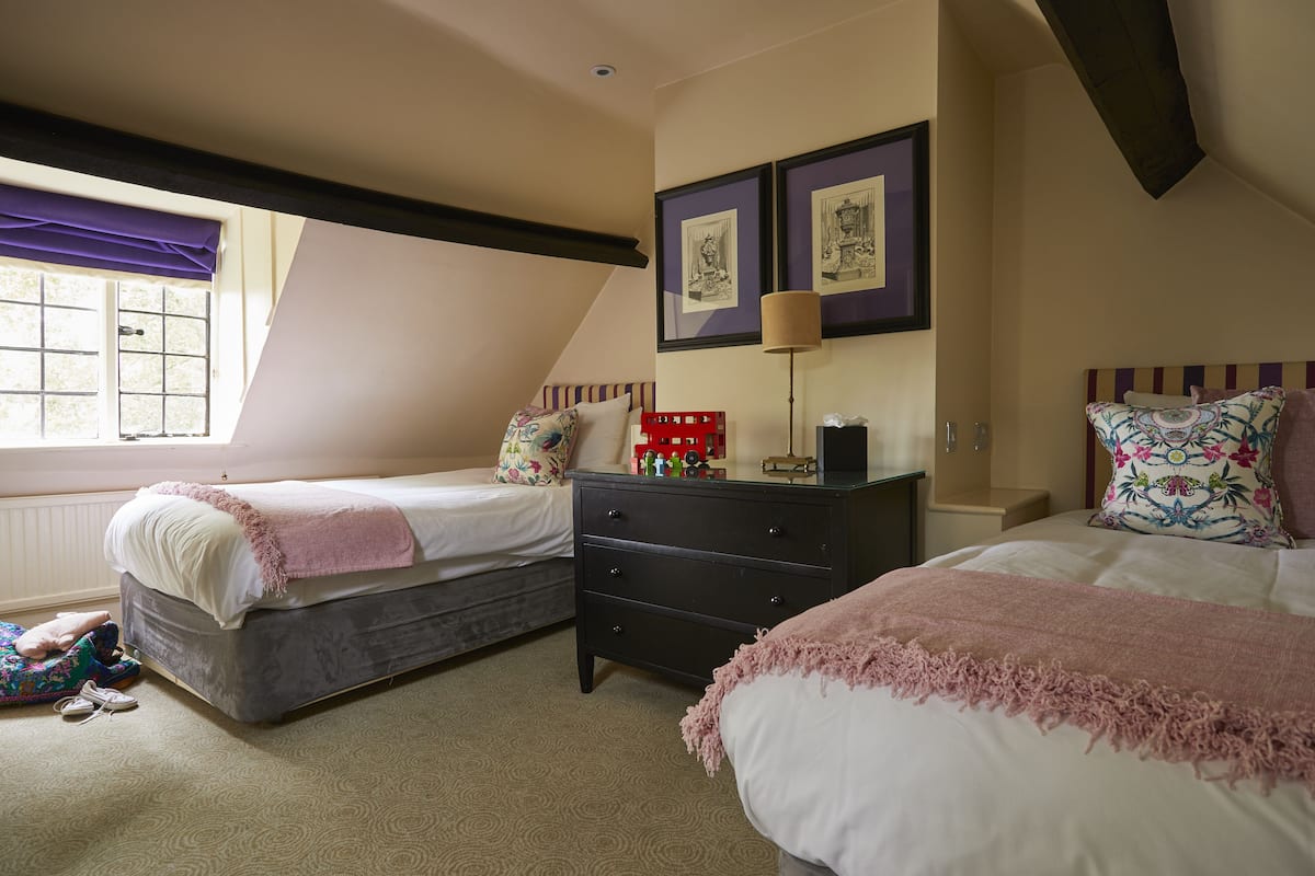 A bedroom with two beds, a dresser, and a window with a purple curtain.