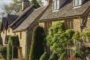 A row of stone houses with steeply pitched roofs, some with ivy, and a well-maintained garden with various shrubs and flowers. - The Slaughters Country Inn (Cheltenham)
