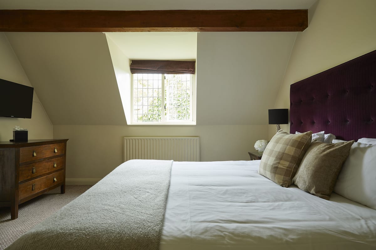 A bedroom with a large bed, a dresser, a window, and a television on the wall.
