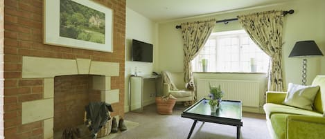 A living room with a fireplace, a television, a sofa, a coffee table, and a window with curtains.