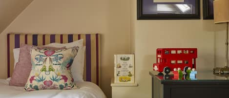 Une chambre à coucher avec un lit, une table de chevet sur laquelle est posé un jouet représentant un autobus à deux étages rouge, et un livre encadré accroché au mur.