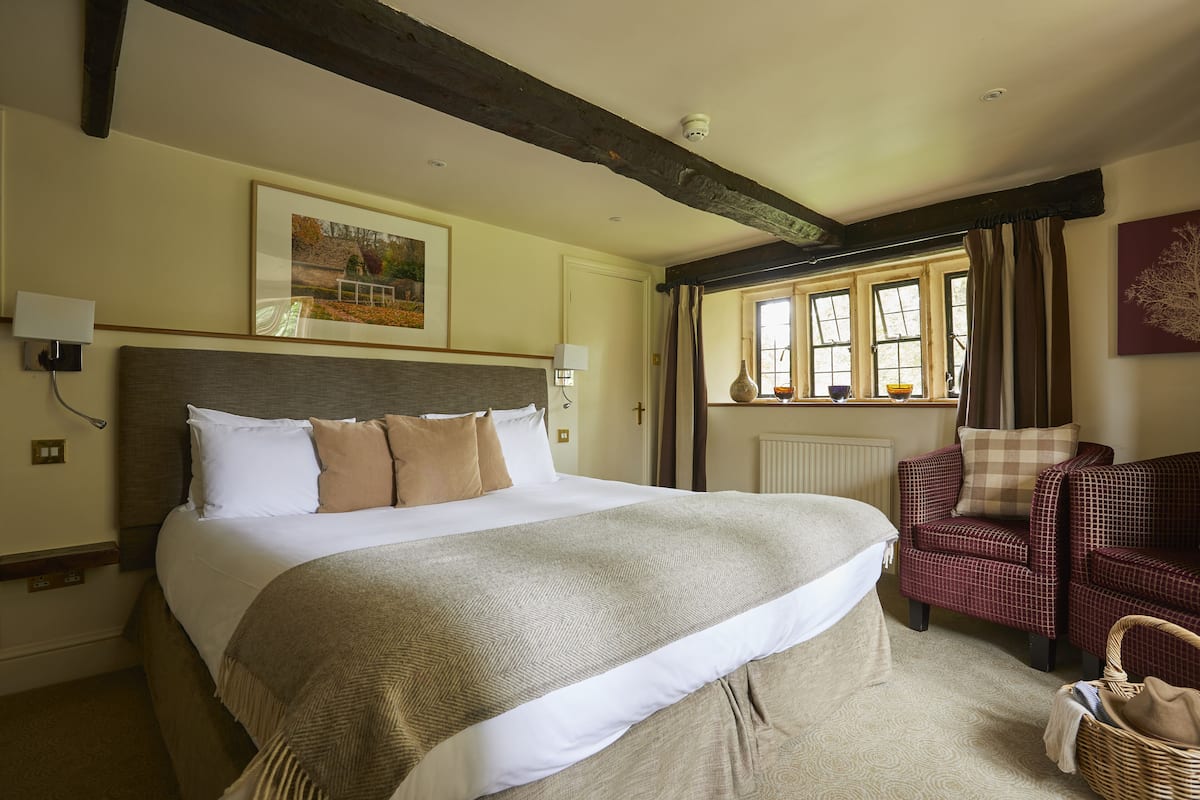 A large bed with a headboard, a red checkered armchair, and a wicker basket on the floor.