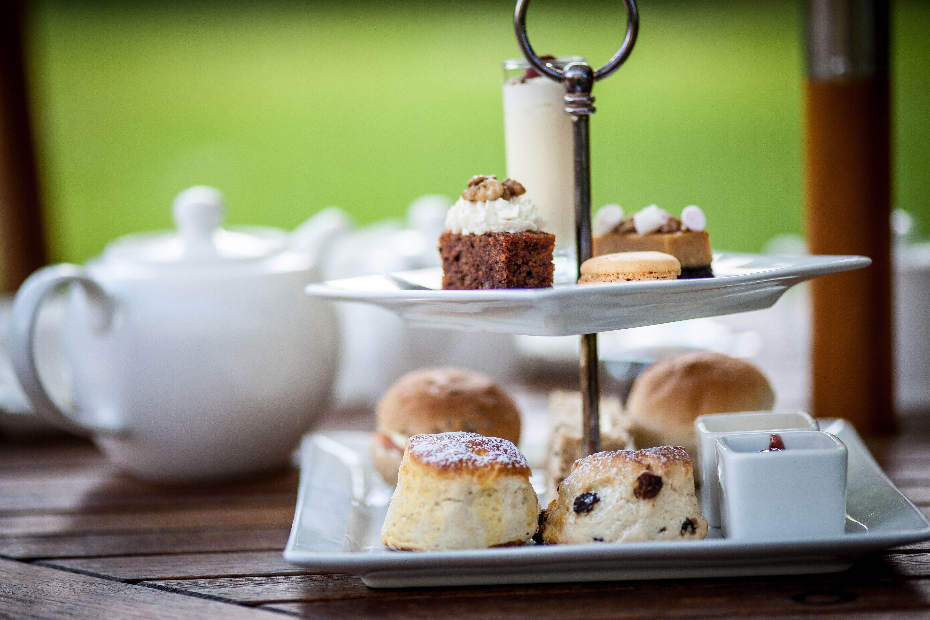 A tray of scones, a cake, and a teapot on a wooden table.