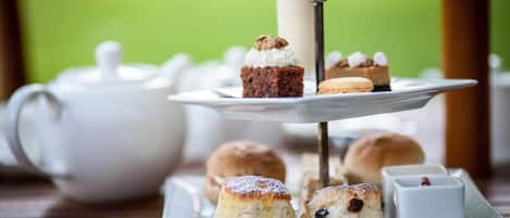 A tray of scones, a cake, and a teapot on a wooden table.