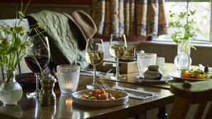 Une table à manger dressée avec des verres à vin, une assiette de nourriture et des vases décoratifs.