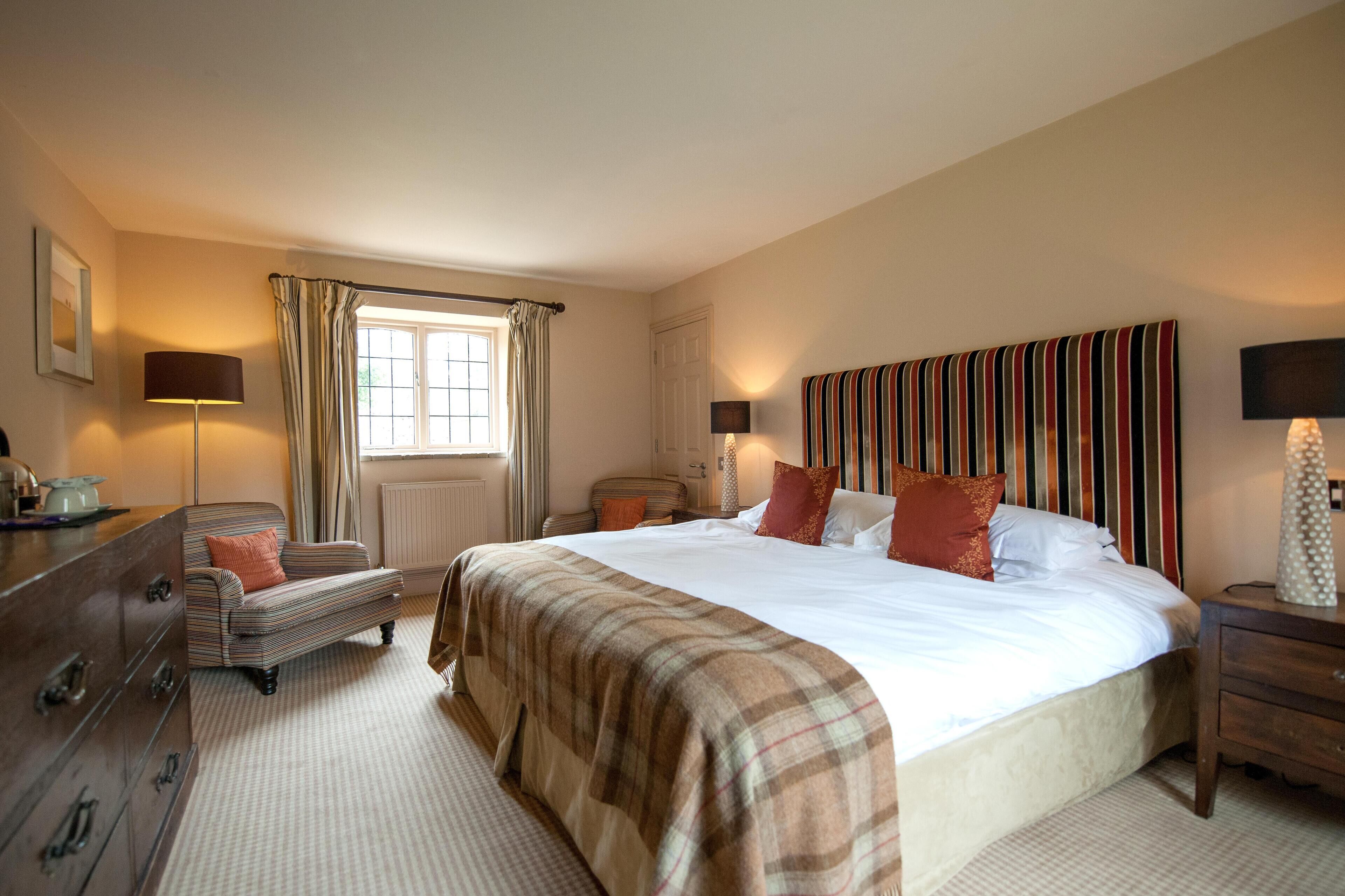 A bedroom with a large bed, a dresser, a nightstand, a lamp, a window with curtains, and a radiator.