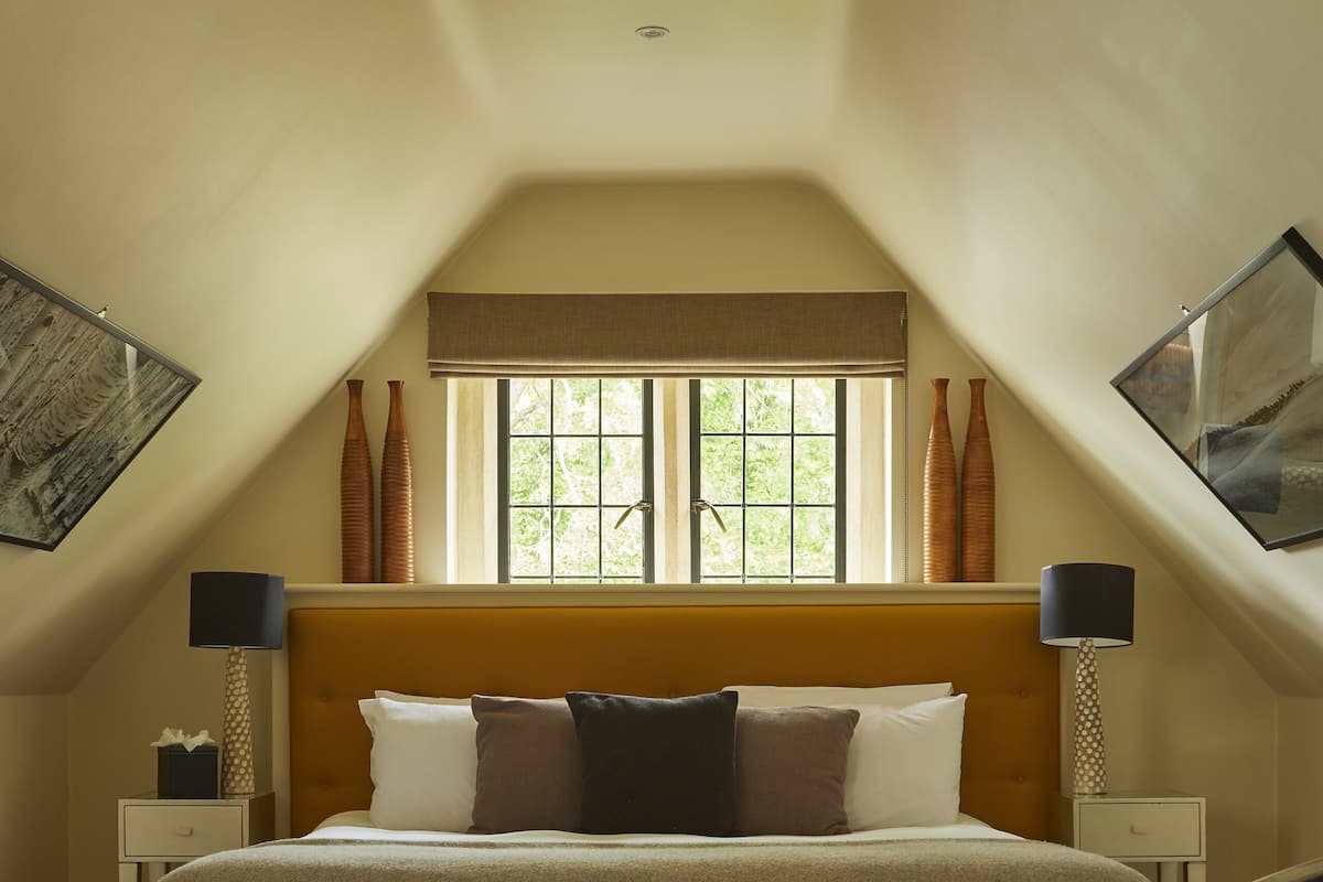 A bedroom with a large bed, a glass-top table with a plant, and a window with curtains.