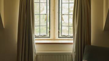 A room with a window, curtains, a radiator, and a chair with a cushion.