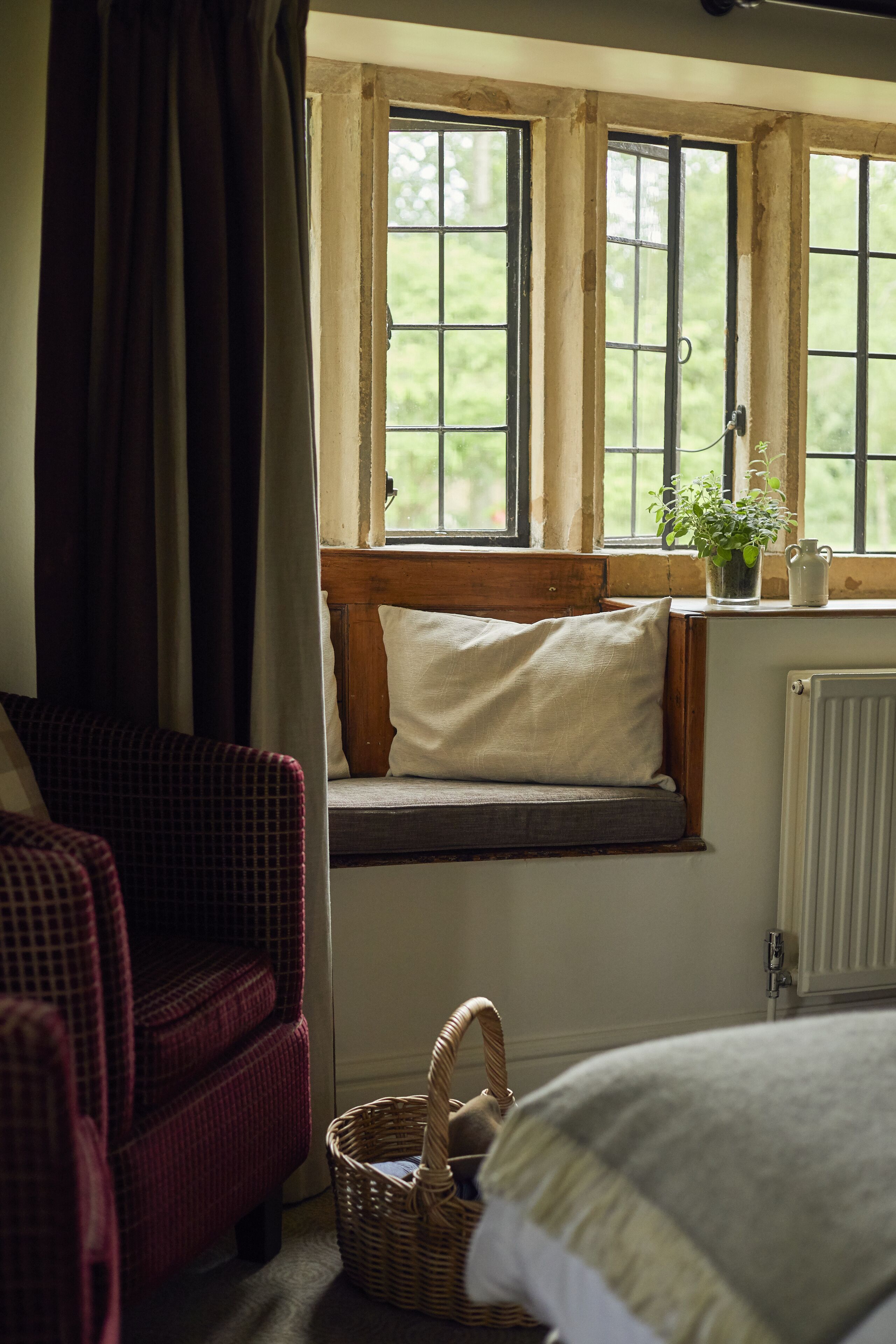 A room with a window seat, a wicker chair, a radiator, and a basket.