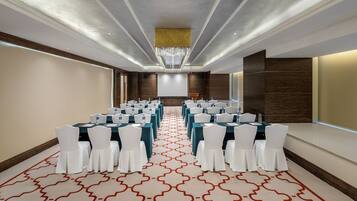 A conference room with rows of tables and chairs, a large screen, and a patterned carpet.