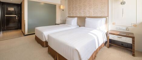 A hotel room with two beds, a large mirror, a bedside table, and a door.