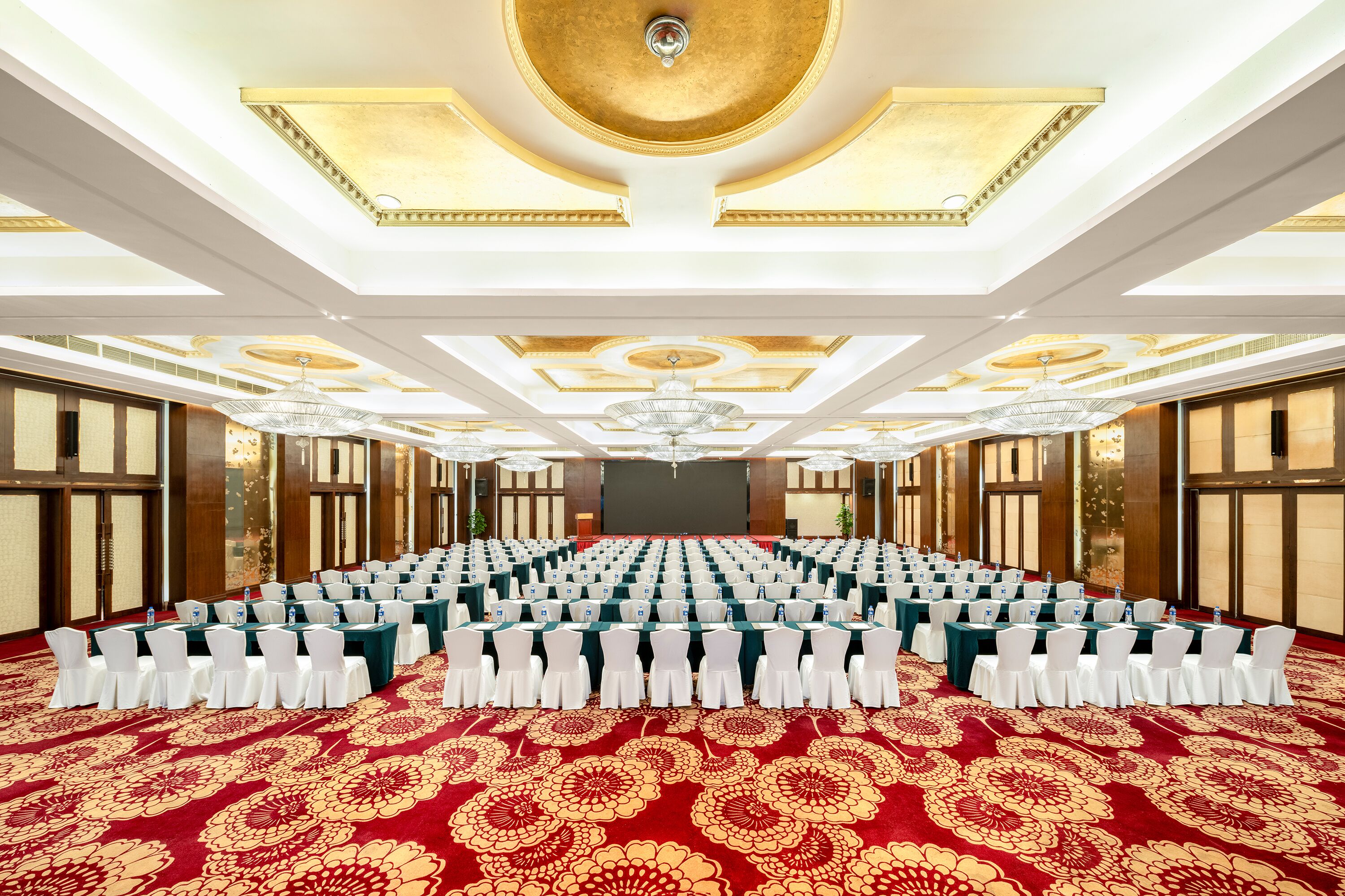 A large conference room with rows of tables and chairs, a patterned carpet, and a decorative ceiling.