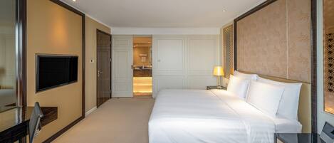 Hotelkamer met een groot bed, een bureau met stoel, een aan de muur bevestigde televisie en een badkamer zichtbaar door een geopende deur.