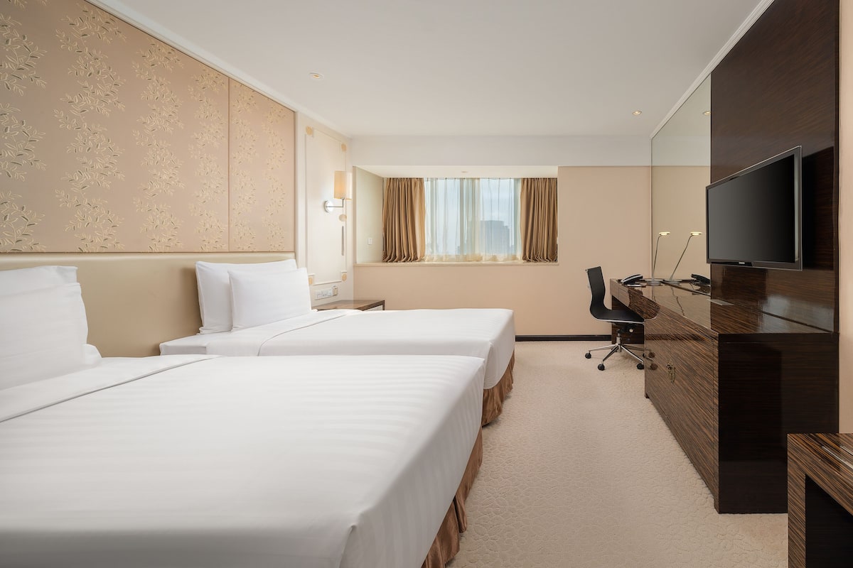 Une chambre d’hôtel avec deux lits, un bureau, une télévision et une fenêtre avec des rideaux.