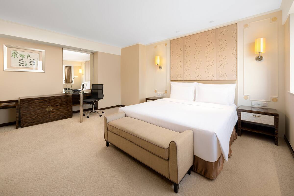 Une chambre d’hôtel avec un grand lit, un bureau, une chaise, une commode et deux tables de chevet avec des lampes.