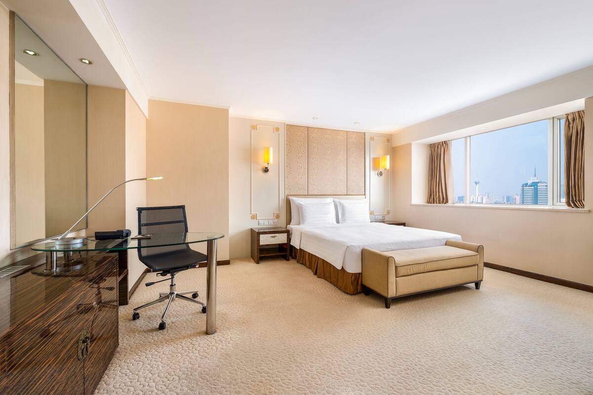 Une chambre d’hôtel comprenant un lit, un bureau avec une chaise, une table de chevet et une fenêtre donnant sur la ville.