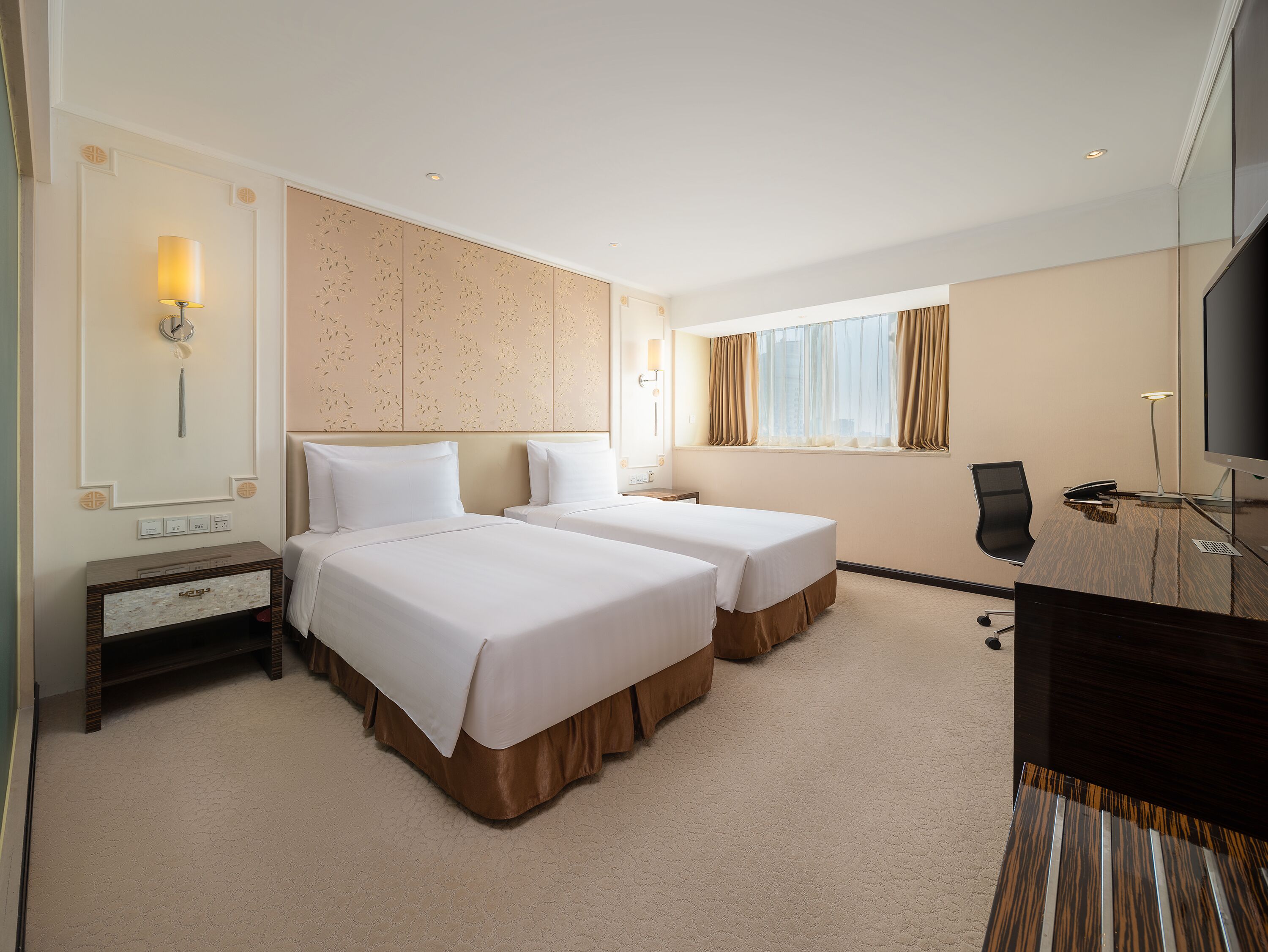 A hotel room with two beds, a desk, a chair, a TV, and a window with curtains.