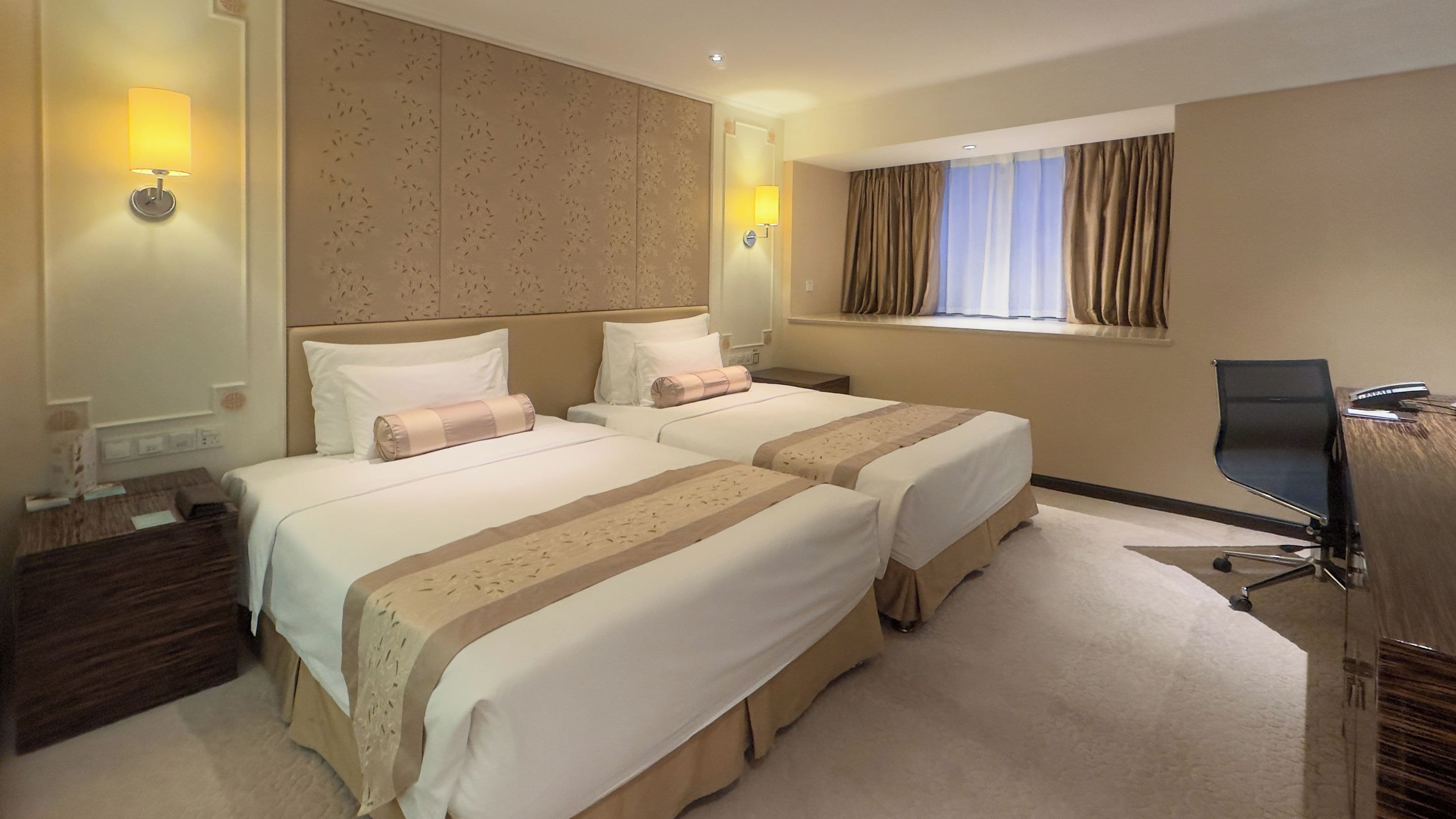 Ein Hotelzimmer mit zwei Betten, einem Schreibtisch, einem Stuhl und einem fenster mit Vorhängen.