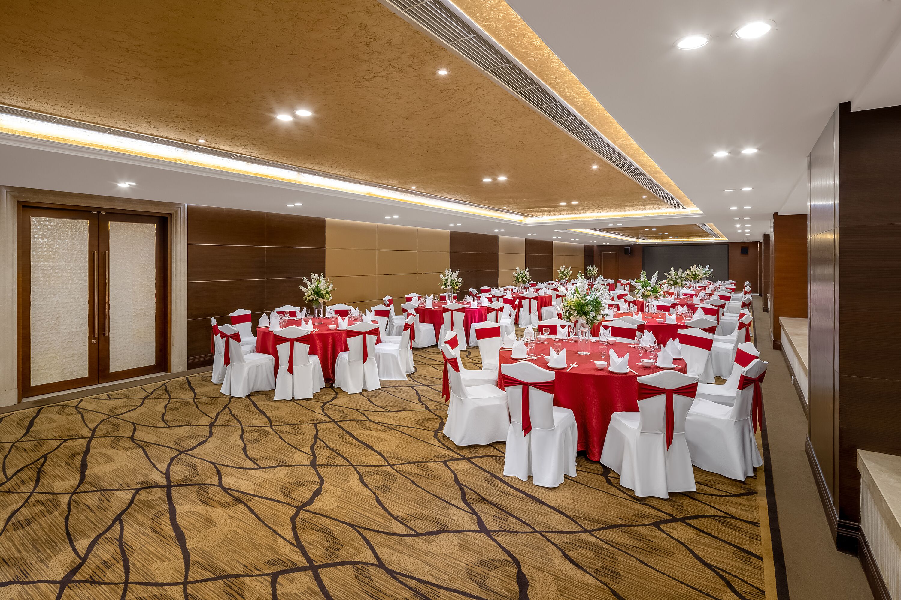 Une grande salle de conférence avec des tables rondes et des chaises blanches, des nappes rouges et un sol recouvert de moquette.