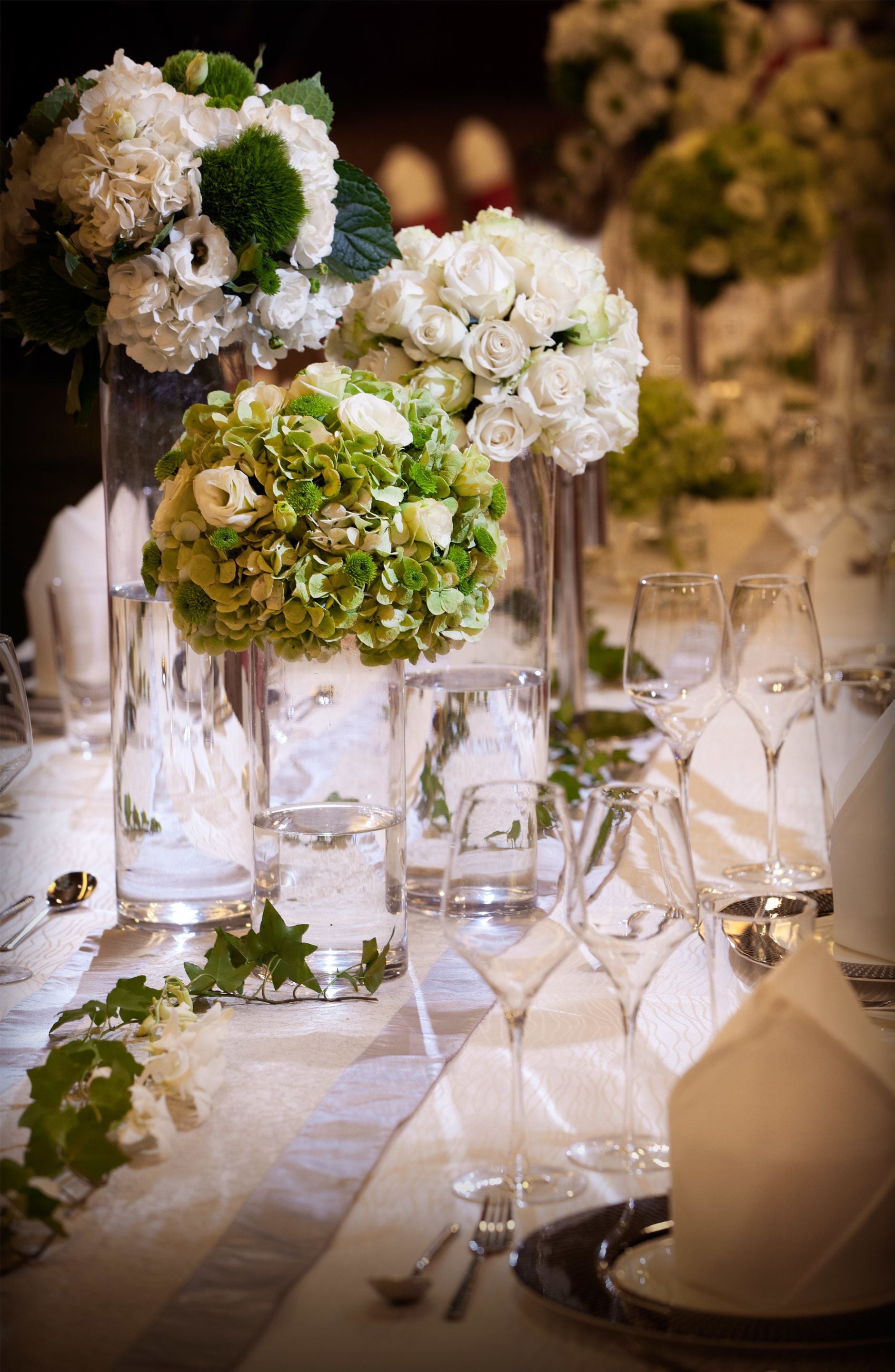 A table set for a formal event with tall glass vases containing white flowers and greenery.