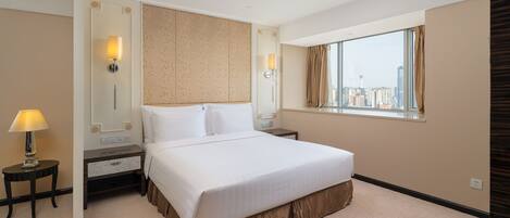 A hotel room with a large bed, a nightstand with a lamp, a mirror, and a window with a city view.