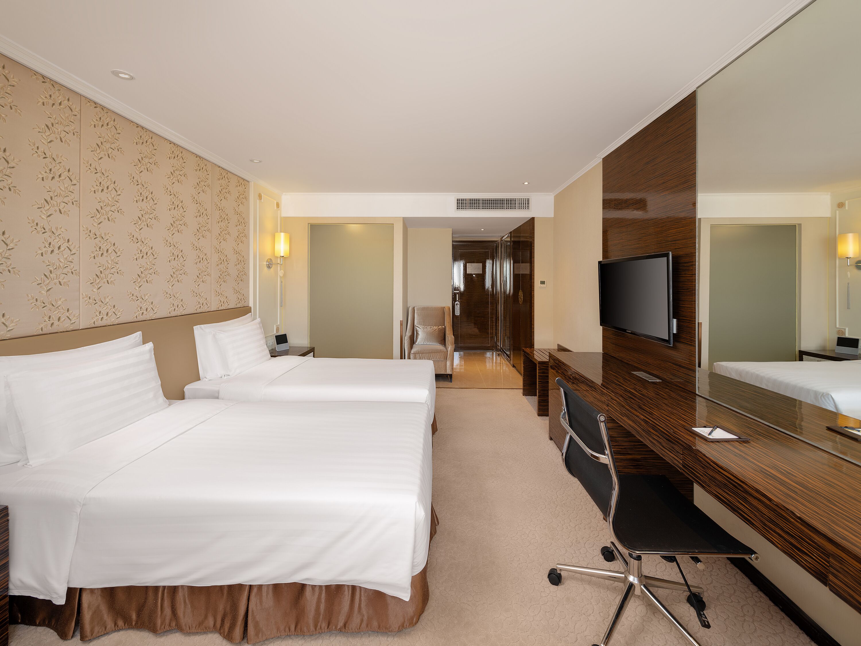 A hotel room with two beds, a desk, a chair, a TV, and a large mirror.