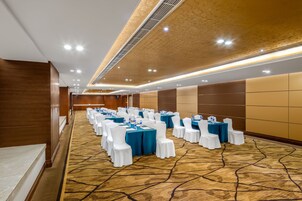 Un salón de conferencias con filas de mesas y sillas, una alfombra estampada y un panel de pared de madera.