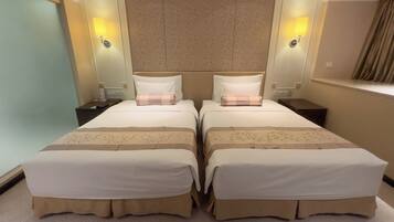 A hotel room with two beds, a headboard with a floral pattern, bedside lamps, and a window with curtains.