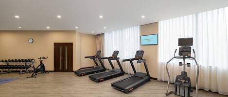 Une salle de sport équipée de tapis de course, d’un vélo d’appartement et d’haltères.
