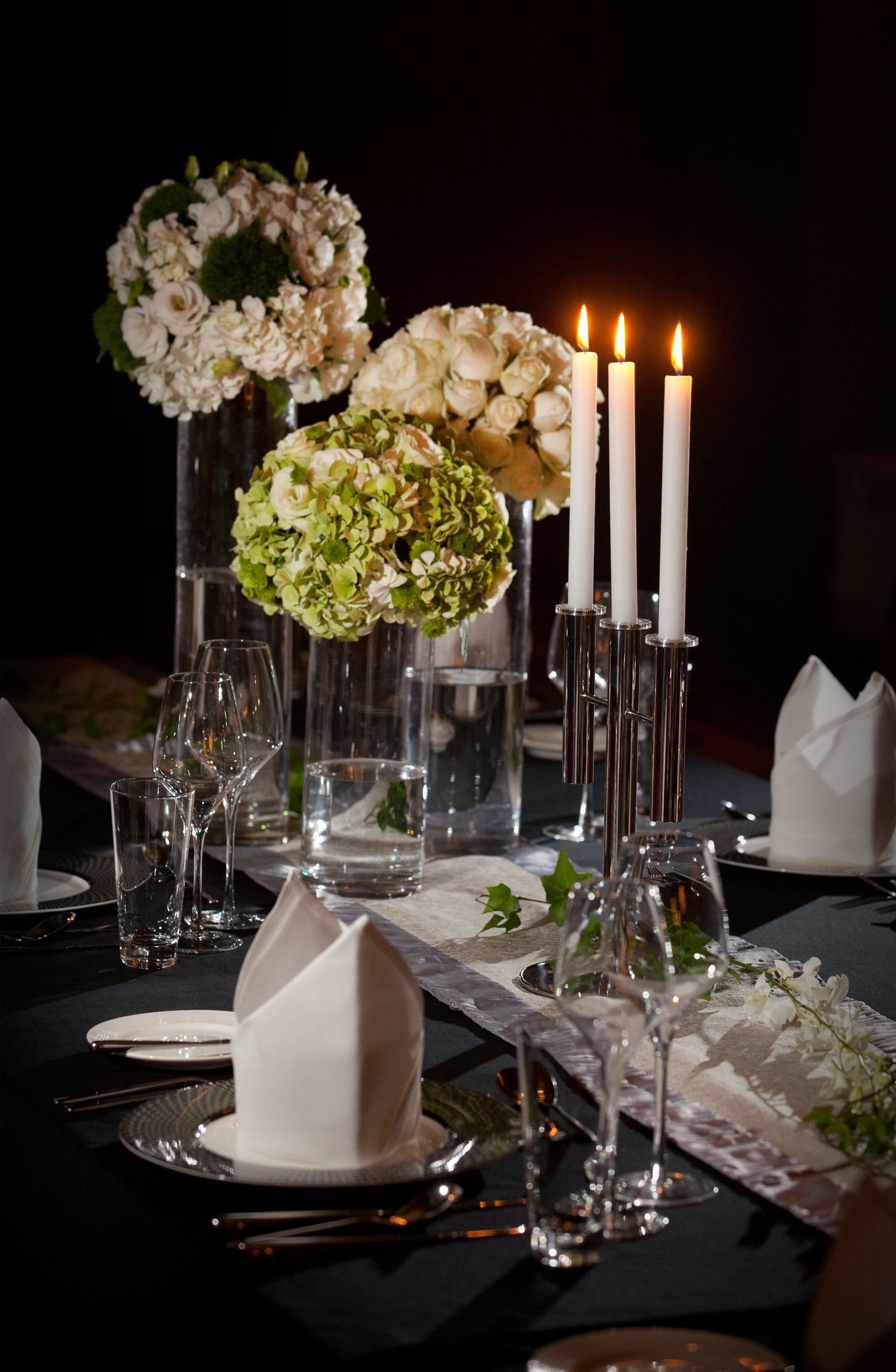 A table set for a formal dinner with clear glassware, white napkins, and floral centerpieces.