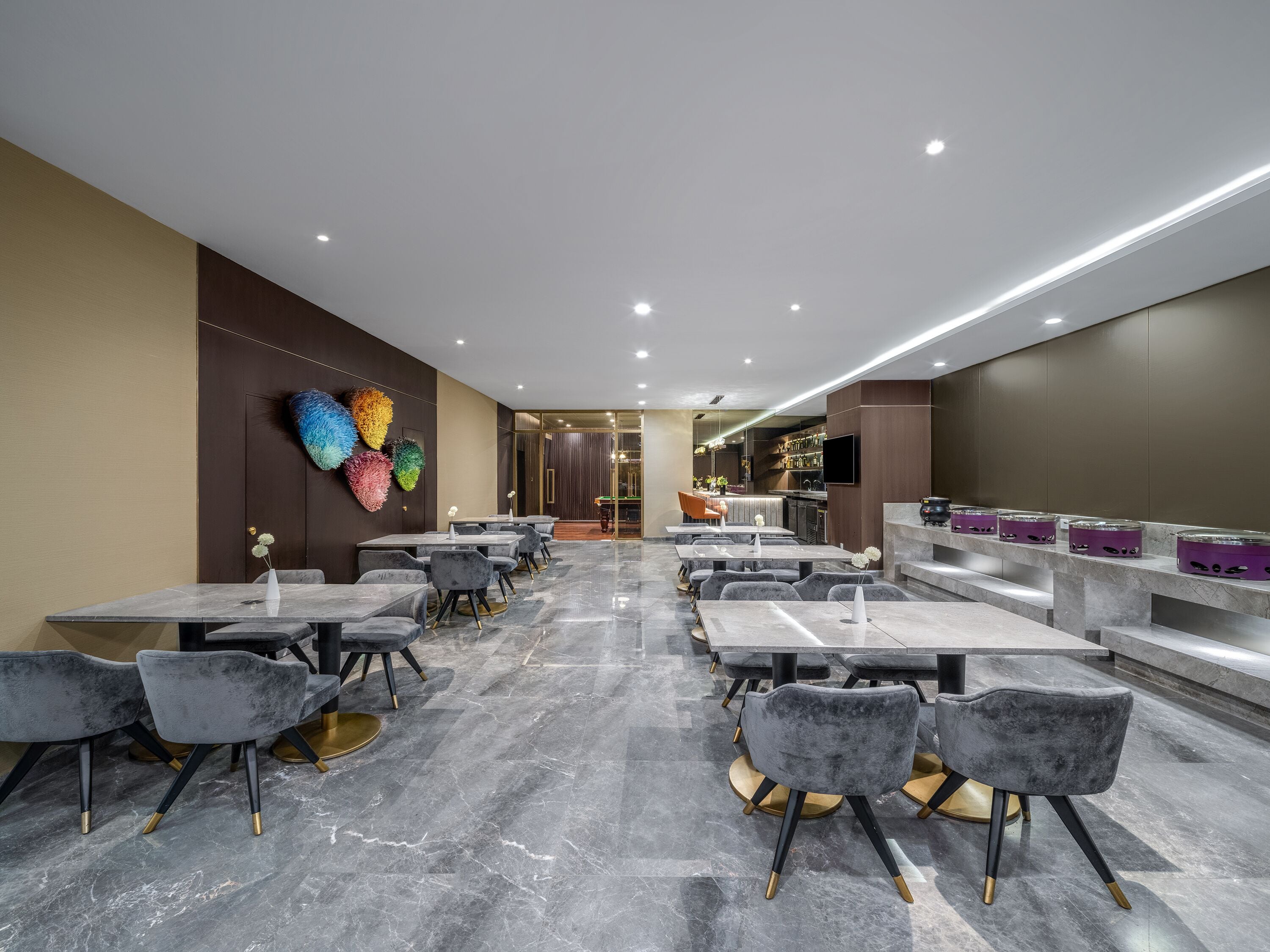 Un restaurante moderno con pisos de mármol, sillas grises tapizadas y una zona de bar con taburetes morados.