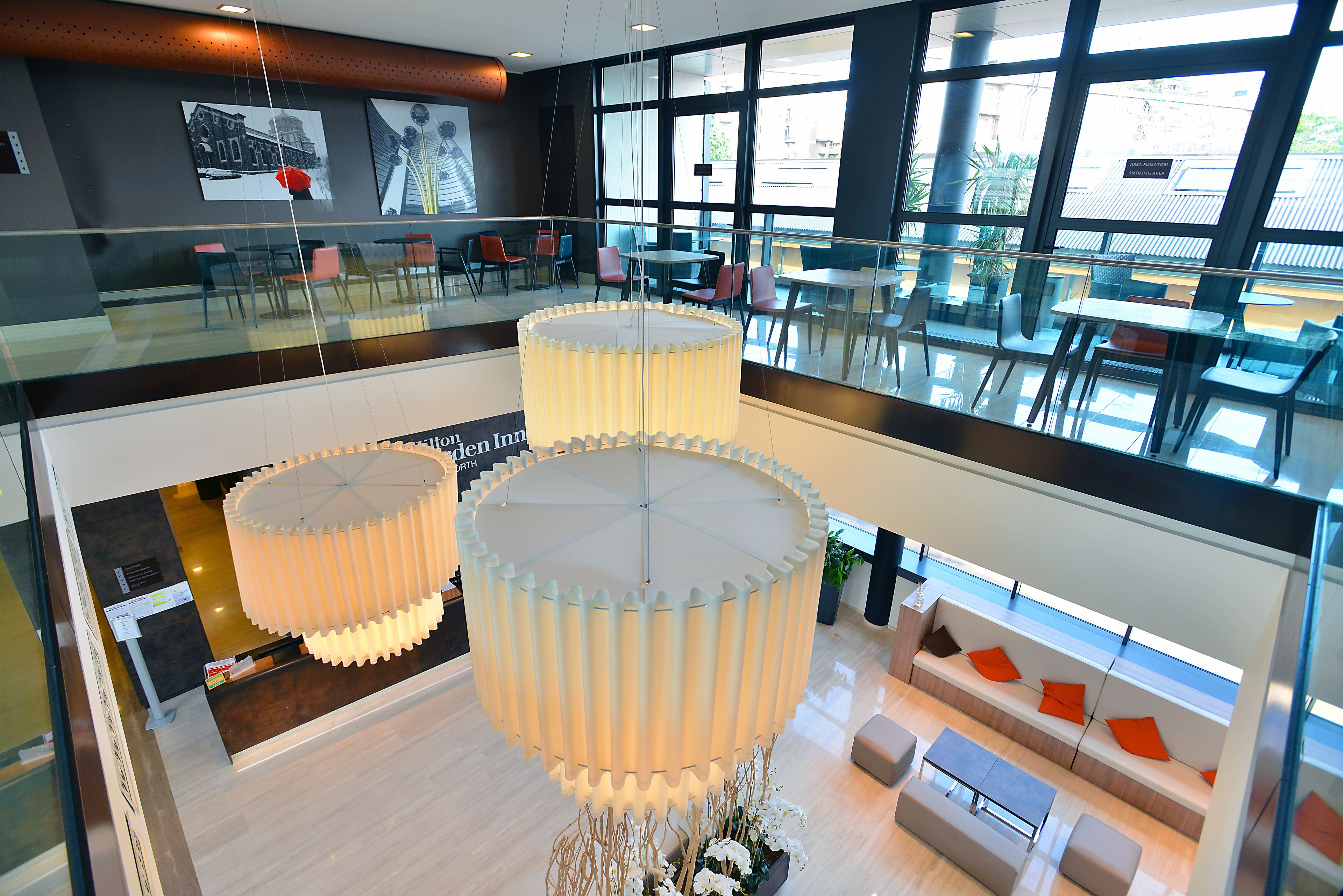 A modern hotel lobby with a glass railing, seating areas, and large floor lamps.