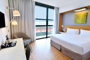 A hotel room with a large bed, a desk with a lamp, a chair, and a window with curtains. - Hilton Garden Inn Milan North (Milan)