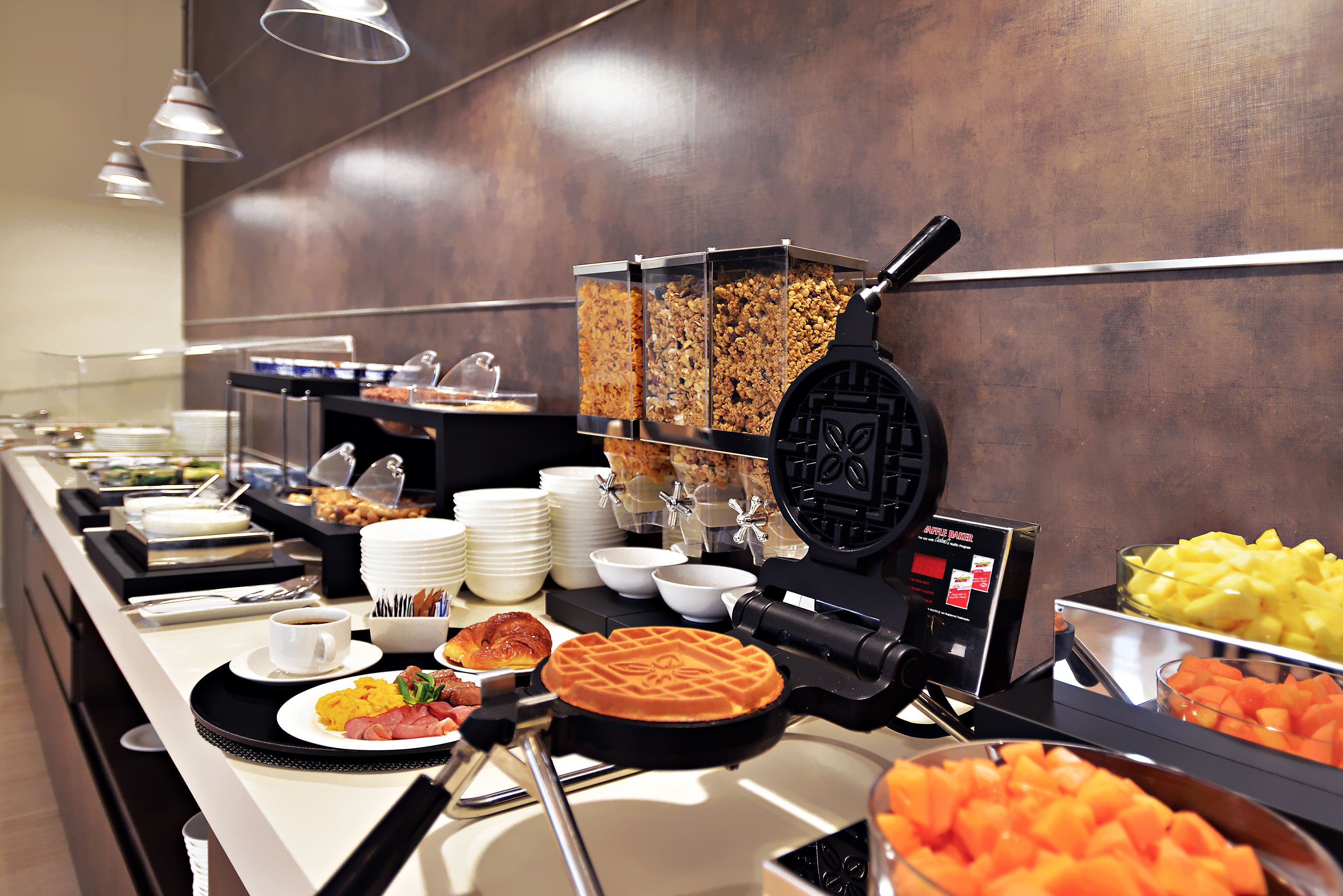 A buffet with various food items, including waffles, fruits, and a waffle iron.