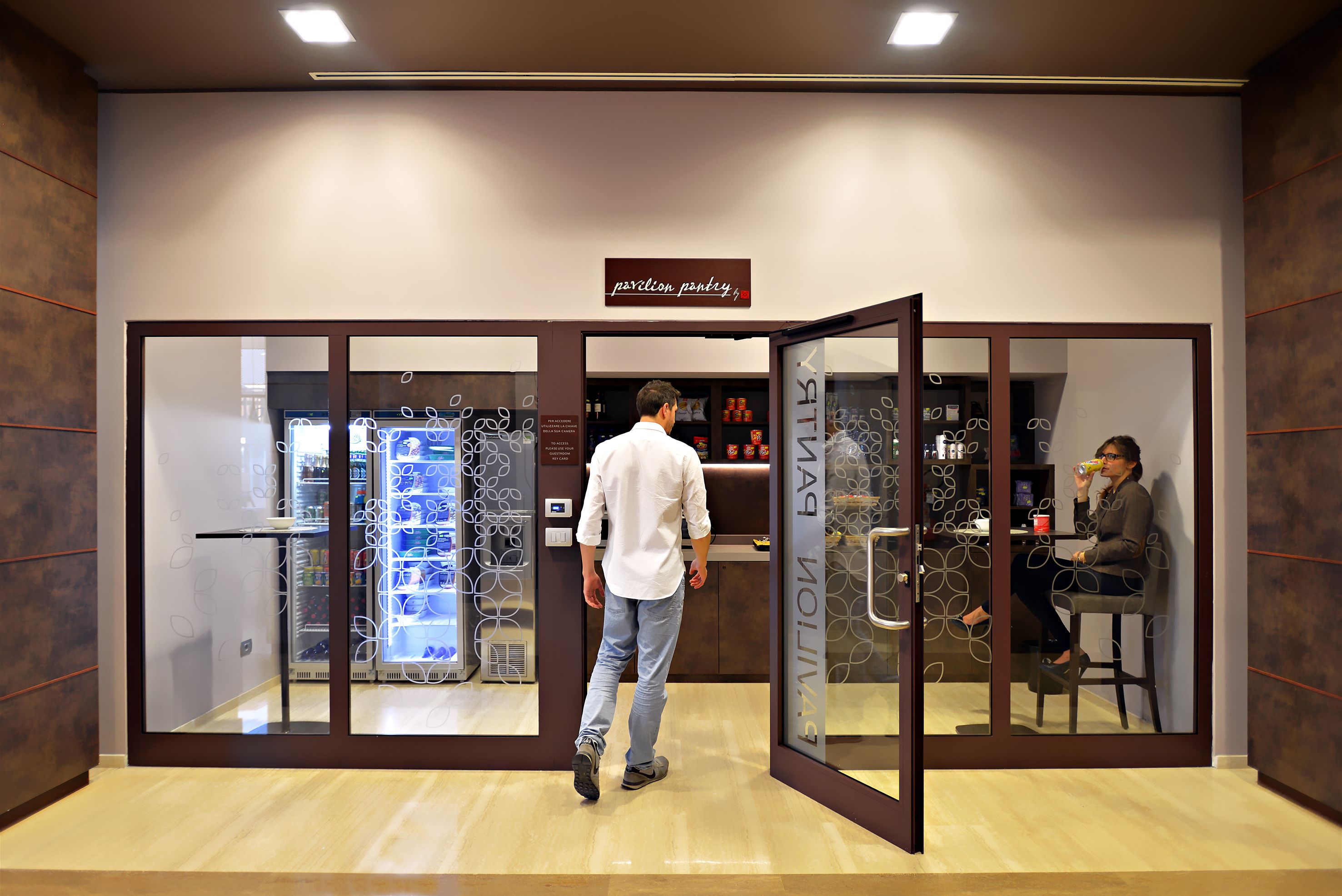 A man walking through a modern, well-lit entrance with a sign reading "pastry pantry". Inside, there are glass display cases and a seating area with a person sitting at a table.