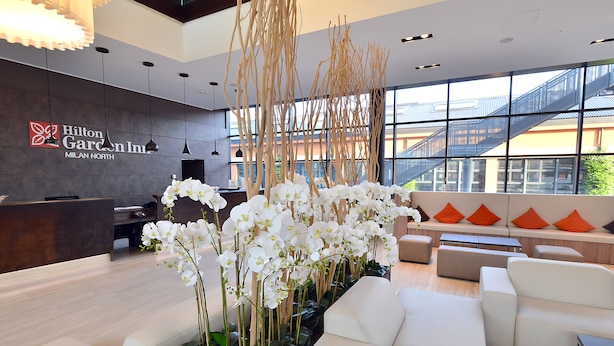 A modern hotel lobby with a reception desk, white sofas, and a large window with a view of a building outside.