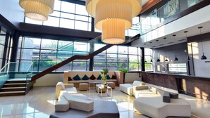 A spacious lobby with a modern staircase, comfortable seating areas, and large windows offering views of the outdoors.