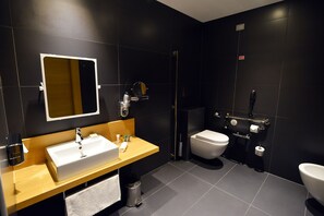 A modern bathroom with a large mirror, a sink, a toilet, and a shower area. - Hilton Garden Inn Milan North (Milan)