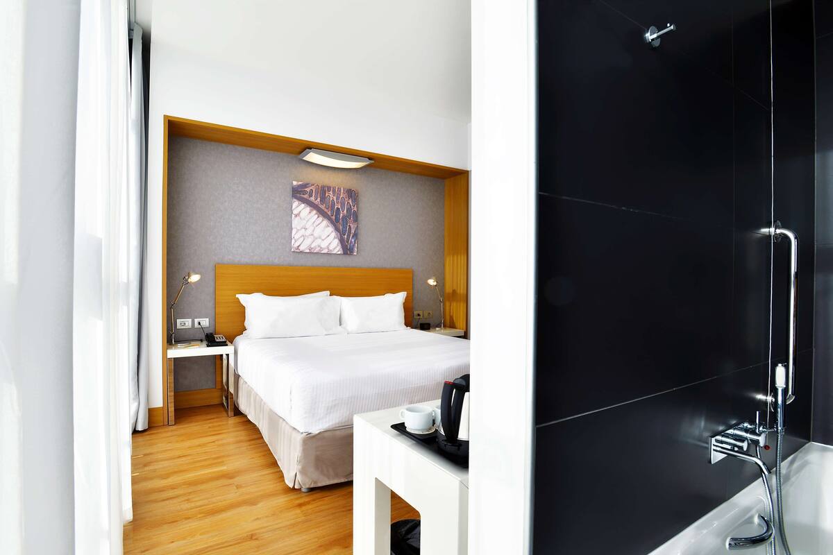 A hotel room with a bed, bedside table, and a shower area.