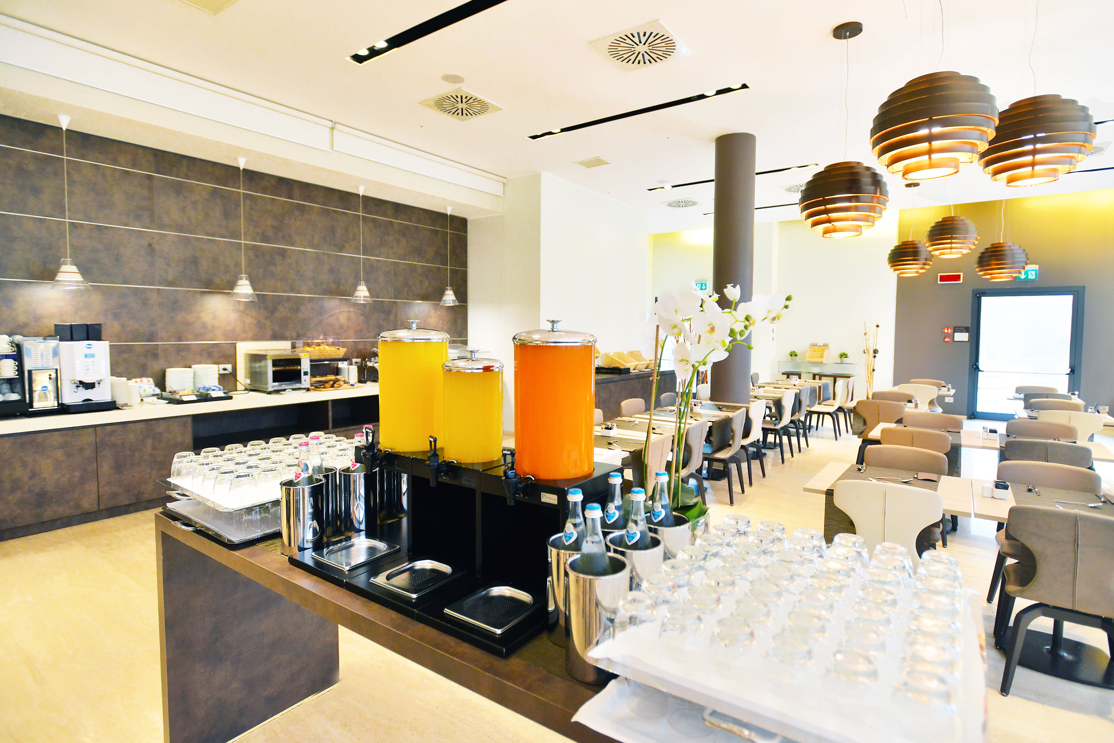 Ein Hotelbuffetbereich mit verschiedenen Getränkespendern, einer Auswahl an Speisen und einer Sitzgelegenheit mit Tischen und Stühlen.