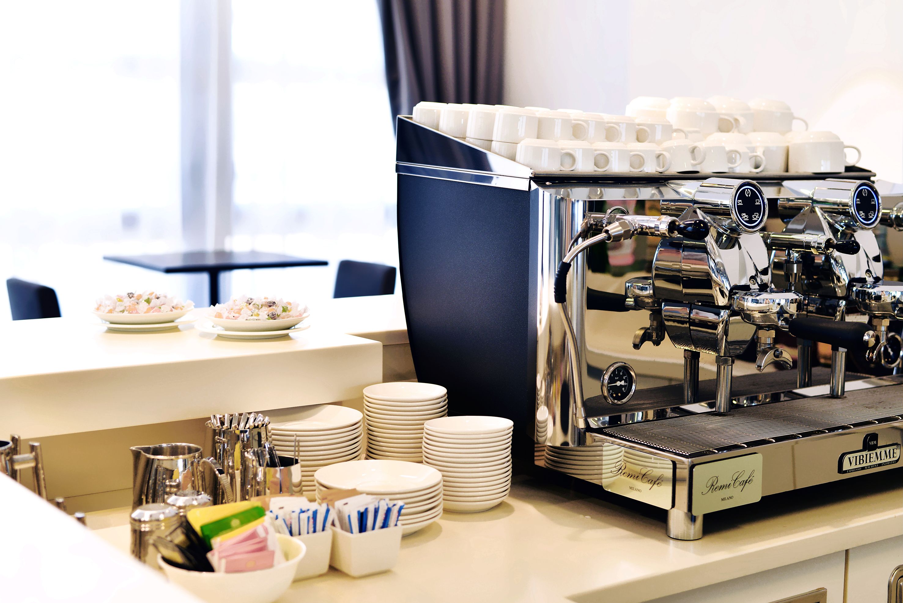 A coffee machine with multiple coffee cups, stacked plates, and utensils on a counter.