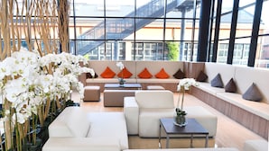 A modern lounge area with white sofas, orange cushions, and a large window offering a view of a building with a metal staircase.