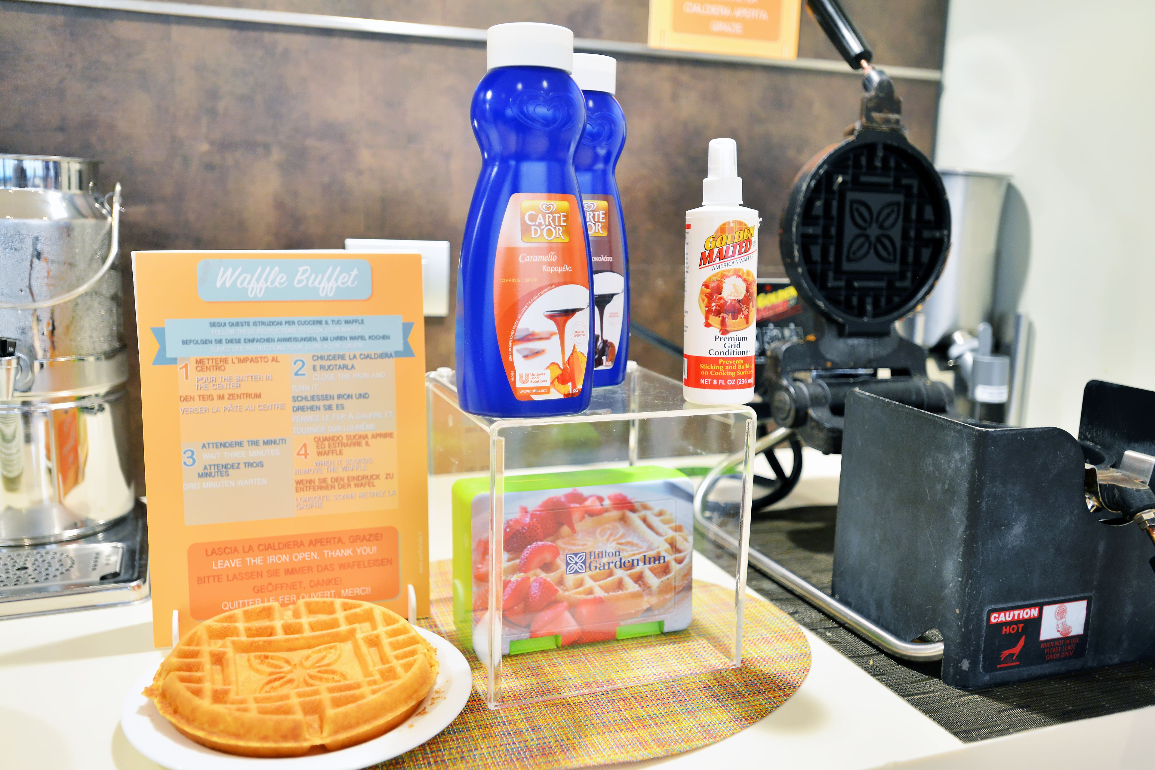 A waffle station with a menu, waffle maker, and condiments.