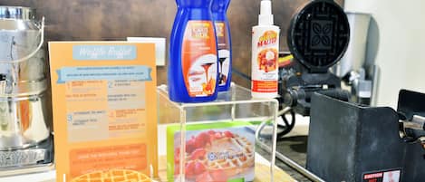 A waffle station with a menu, waffle maker, and condiments.