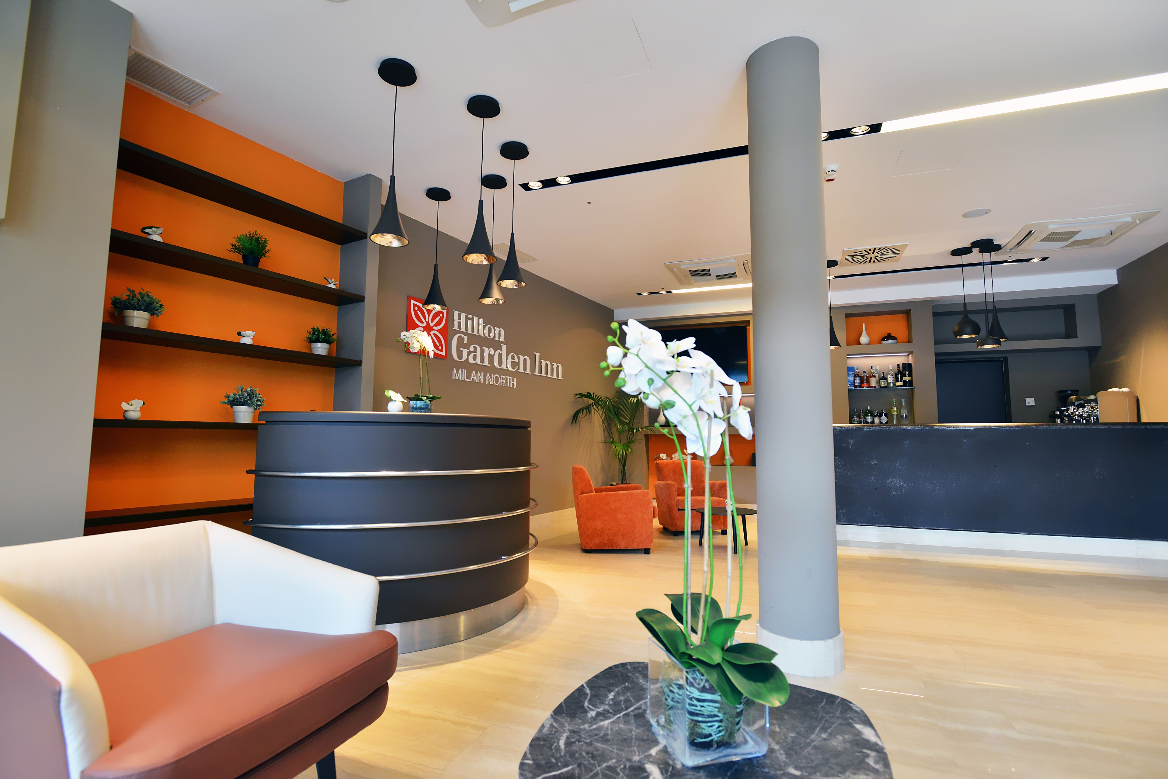 A hotel reception area with a curved reception desk, multiple seating options, and a potted plant.