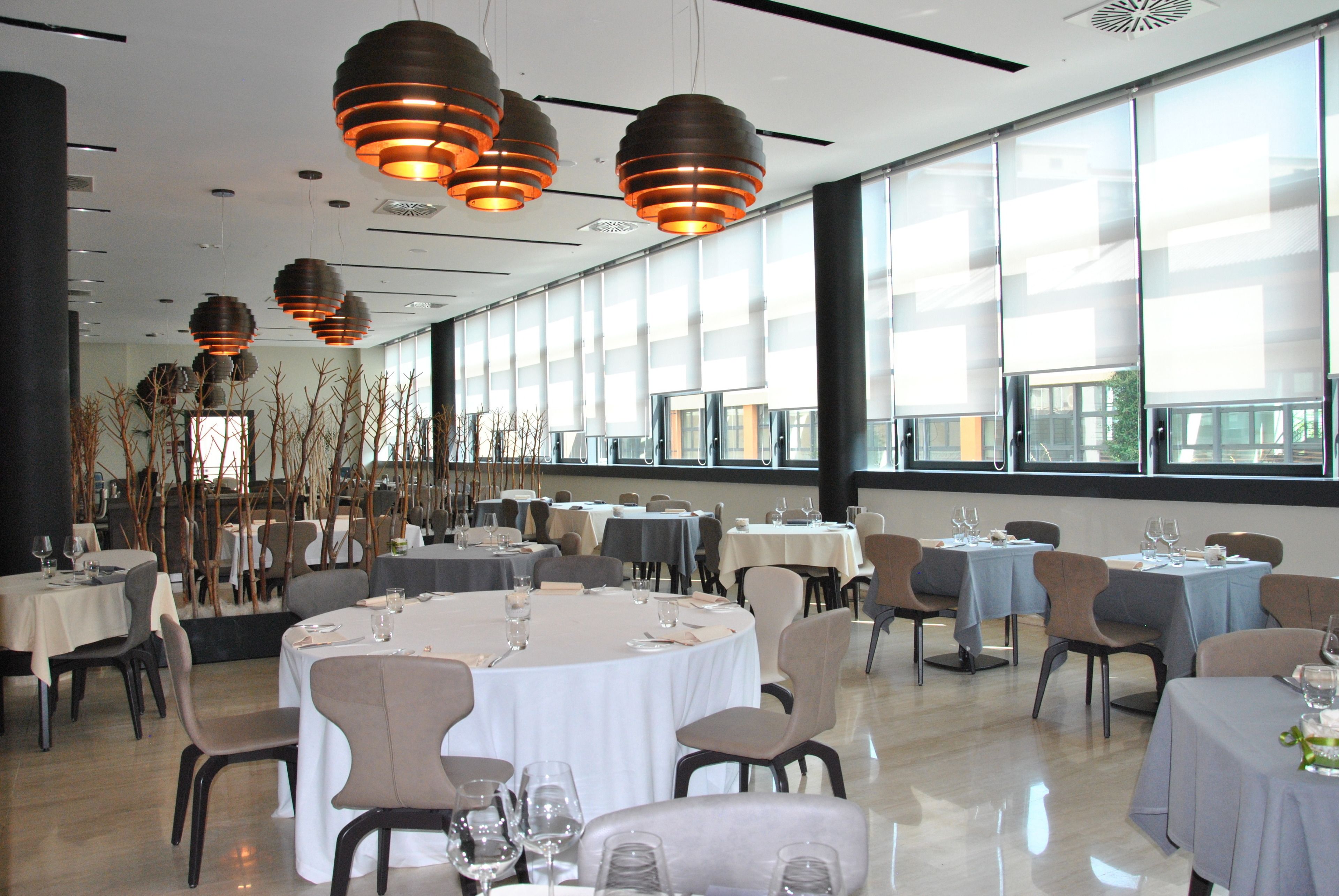 A spacious dining area with round tables, chairs, and hanging pendant lights.