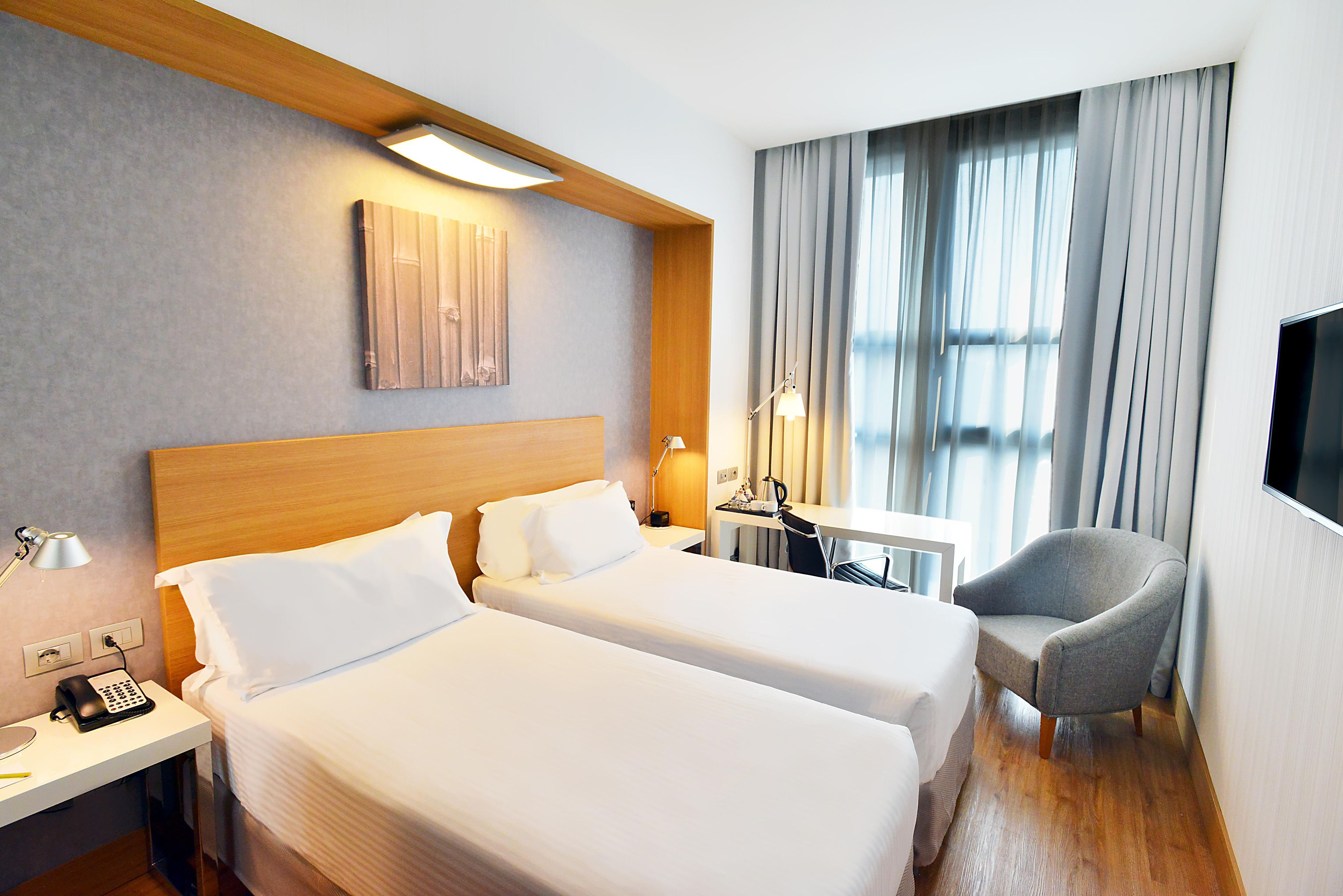 Habitación de hotel con dos camas, un escritorio con teléfono, una silla y un televisor fijado a la pared.