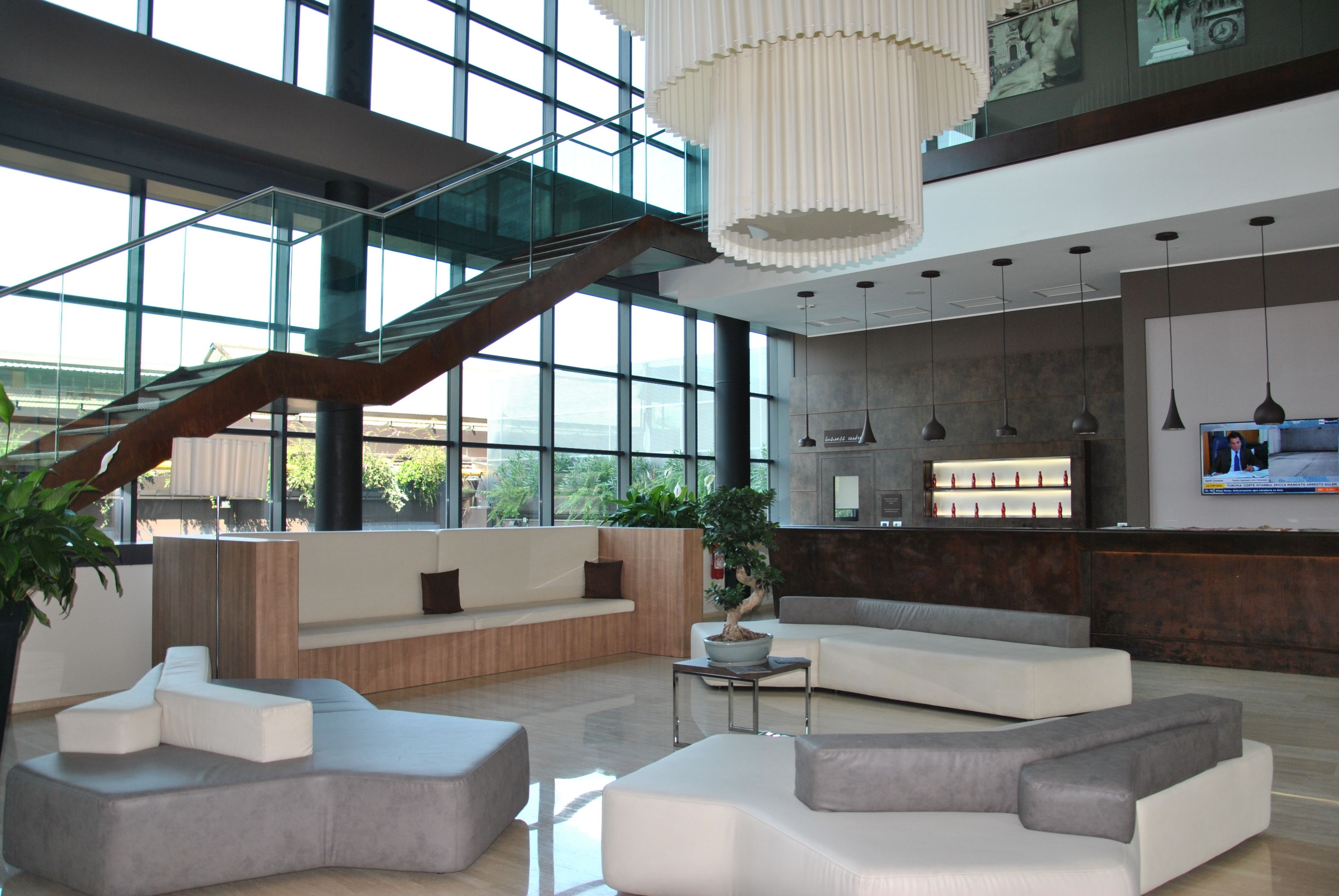 Um hall amplo com escadaria moderna, áreas de estar e balcão de recepção.