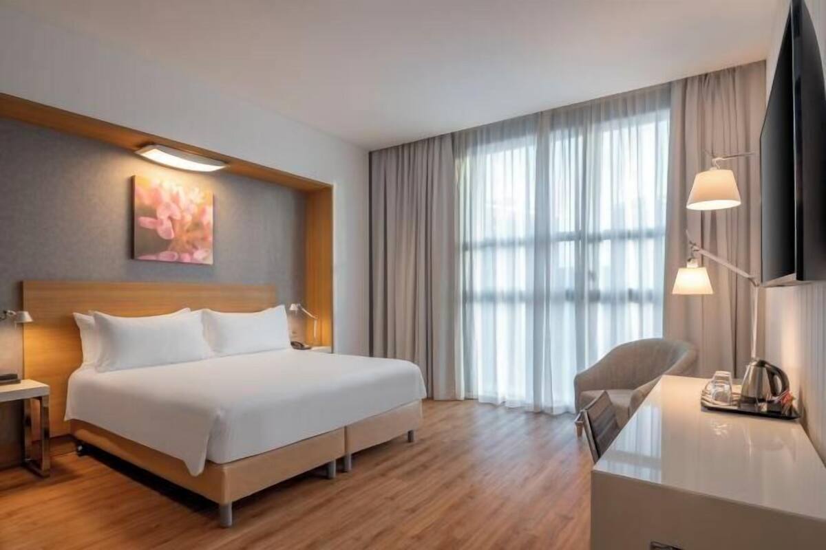 A hotel room with a bed, bedside table, lamp, desk, chair, and a TV.